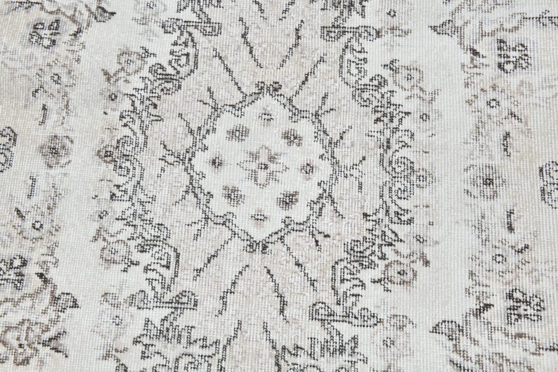 Peut inclure: Un tapis blanc avec un motif floral noir et gris. Le tapis a un aspect vieilli, avec certaines parties du noir et du gris d&eacute;lav&eacute;es.