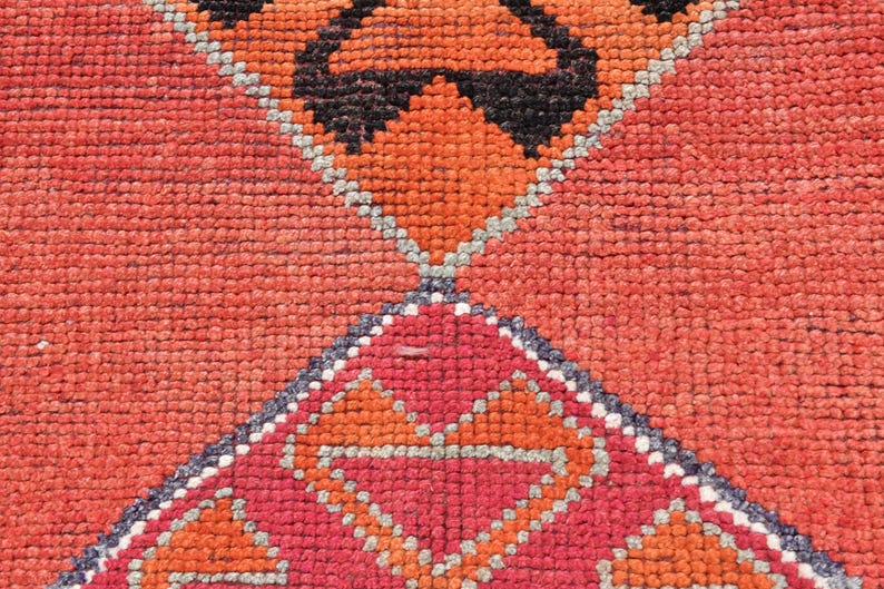 May include: Close-up of a red, orange, and gray patterned rug with a geometric design. The rug is woven with a variety of textures and colors.