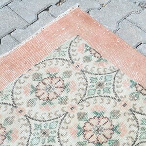 May include: A vintage rug with a peach border and a white center with a floral pattern in shades of pink, green, and gray.