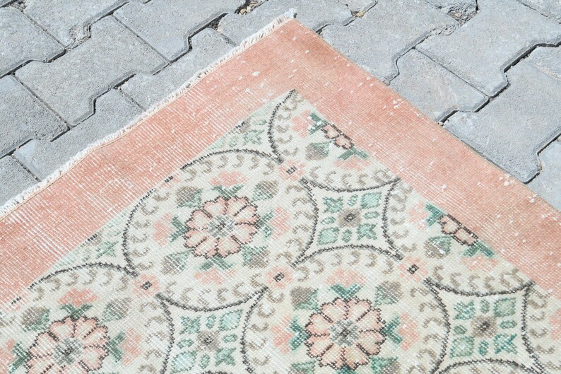 May include: A vintage rug with a peach border and a white center with a floral pattern in shades of pink, green, and gray.