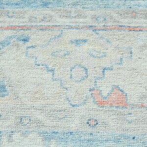 K&ouml;nnte beinhalten: Nahaufnahme eines wei&szlig;en Teppichs mit einem blauen und rosafarbenen geometrischen Muster. Der Teppich hat einen abgenutzten, Vintage-Look.