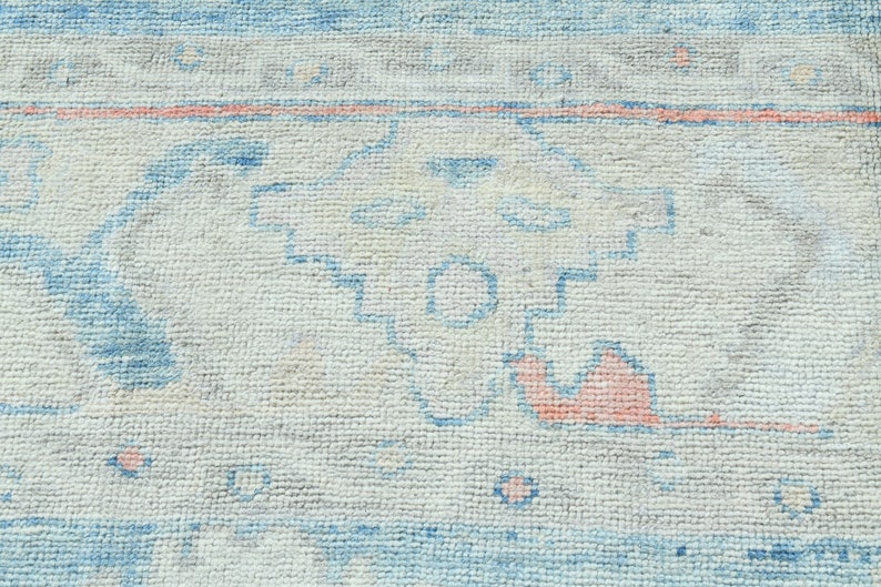 K&ouml;nnte beinhalten: Nahaufnahme eines wei&szlig;en Teppichs mit einem blauen und rosafarbenen geometrischen Muster. Der Teppich hat einen abgenutzten, Vintage-Look.