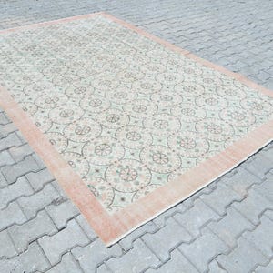 May include: A vintage rug with a cream background and a repeating pattern of light green and pink floral motifs. The rug has a peach-colored border.