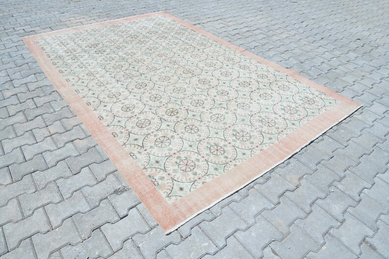 May include: A vintage rug with a cream background and a repeating pattern of light green and pink floral motifs. The rug has a peach-colored border.