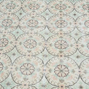 May include: A vintage rug with a repeating pattern of light pink and green floral motifs on a cream background.