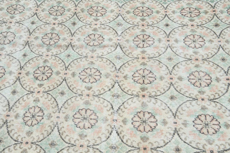 May include: A vintage rug with a repeating pattern of light pink and green floral motifs on a cream background.
