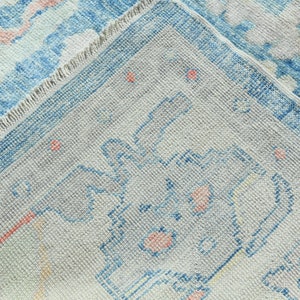 K&ouml;nnte beinhalten: Nahaufnahme eines hellblauen und wei&szlig;en Teppichs mit einem verblassten Blumenmuster. Der Teppich hat einen Fransenrand und eine strukturierte Webart.