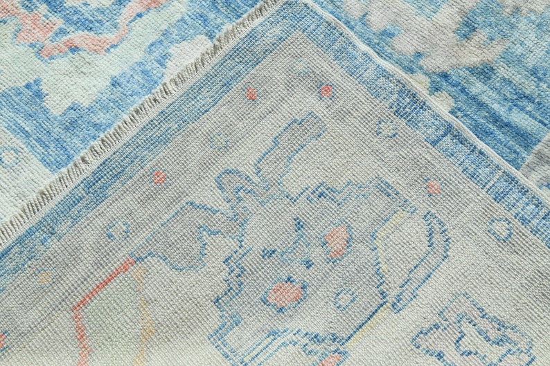 K&ouml;nnte beinhalten: Nahaufnahme eines hellblauen und wei&szlig;en Teppichs mit einem verblassten Blumenmuster. Der Teppich hat einen Fransenrand und eine strukturierte Webart.
