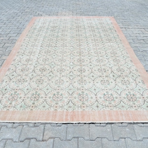 May include: A vintage rug with a light green and cream background and a repeating pattern of pink and green floral motifs. The rug has a peach-colored border.