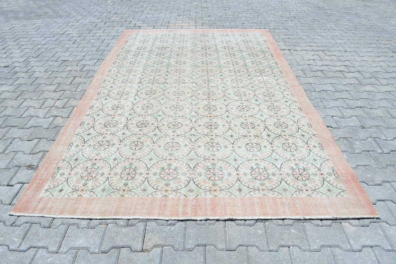 May include: A vintage rug with a light green and cream background and a repeating pattern of pink and green floral motifs. The rug has a peach-colored border.