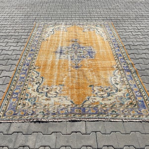 May include: A vintage rug with a faded orange background and a blue and white floral pattern. The rug has a fringed edge.