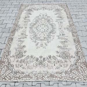 Peut inclure: Un tapis vintage de couleur cr&egrave;me avec un motif floral brun. Le tapis a un aspect vieilli et est parfait pour ajouter une touche de charme vintage &agrave; n'importe quelle pi&egrave;ce.
