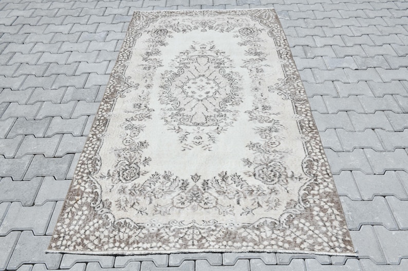 Peut inclure: Un tapis vintage de couleur cr&egrave;me avec un motif floral brun. Le tapis a un aspect vieilli et est parfait pour ajouter une touche de charme vintage &agrave; n'importe quelle pi&egrave;ce.