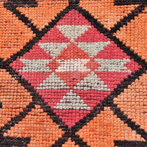 May include: Close-up of a colorful woven rug with a geometric pattern in shades of orange, pink, white, and black.