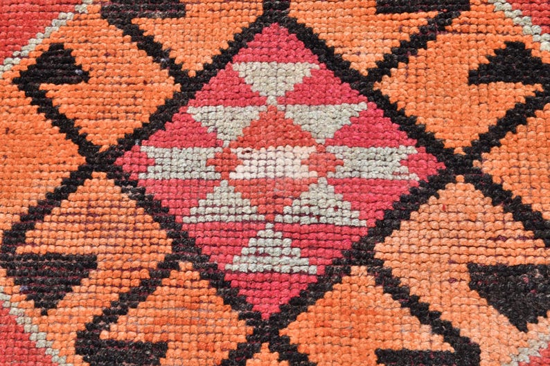 May include: Close-up of a colorful woven rug with a geometric pattern in shades of orange, pink, white, and black.
