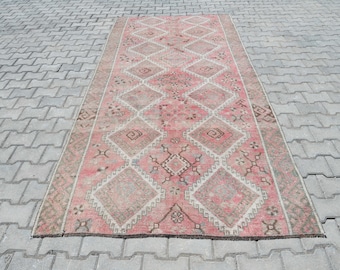 May include: A pink and white vintage rug with a diamond pattern. The rug has a distressed look and is made of wool.