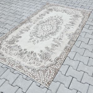 Peut inclure: Un tapis vintage blanc avec un motif floral brun. Le tapis a un aspect vieilli et est parfait pour ajouter une touche de charme vintage &agrave; n'importe quelle pi&egrave;ce.