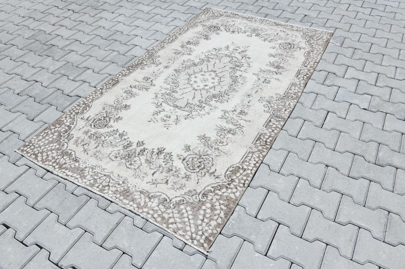 Peut inclure: Un tapis vintage blanc avec un motif floral brun. Le tapis a un aspect vieilli et est parfait pour ajouter une touche de charme vintage &agrave; n'importe quelle pi&egrave;ce.
