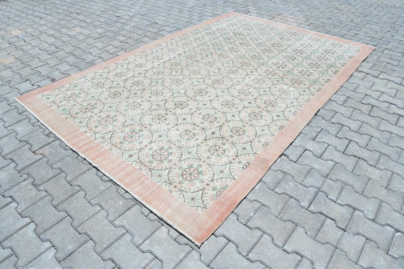 May include: A vintage rug with a cream background and a pink border. The rug has a repeating pattern of floral motifs in shades of green, pink, and white.