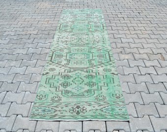 May include: A green and white vintage kilim rug with a geometric pattern. The rug is laid out on a gray concrete surface.