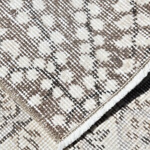 Peut inclure: Gros plan sur un tapis &agrave; motifs blancs et bruns avec une bordure frang&eacute;e. Le tapis a une texture tiss&eacute;e et un motif g&eacute;om&eacute;trique subtil.