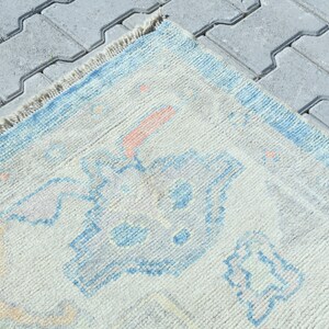 K&ouml;nnte beinhalten: Ein hellblauer und cremefarbener Teppich mit geometrischem Muster. Der Teppich hat einen Fransenrand.