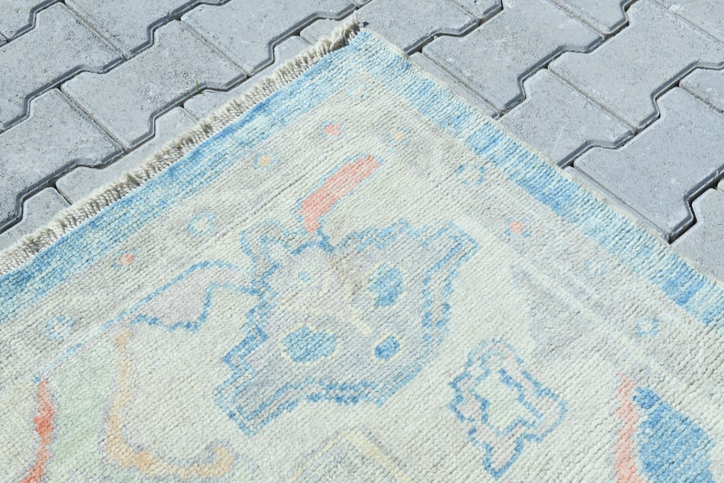 K&ouml;nnte beinhalten: Ein hellblauer und cremefarbener Teppich mit geometrischem Muster. Der Teppich hat einen Fransenrand.