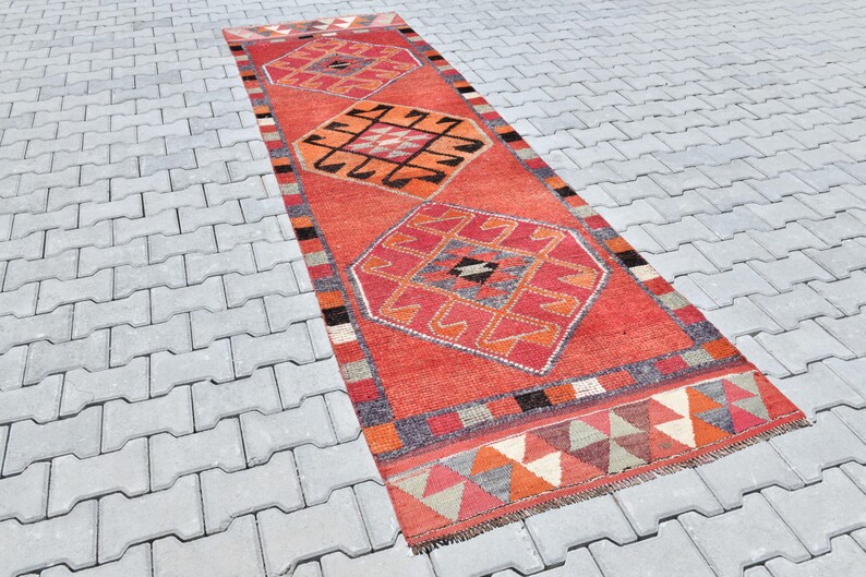 May include: A red, orange, and gray patterned rug with a geometric design. The rug is laid out on a gray concrete surface.