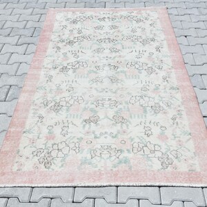 Può includere: Un tappeto vintage con un motivo floreale in tonalità rosa, bianco e verde. Il tappeto ha un aspetto vissuto e un bordo rosa.