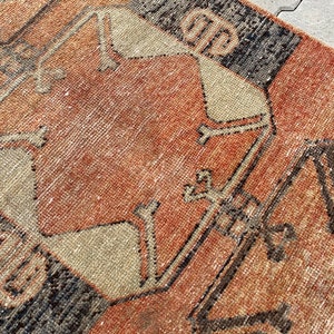 Pu&ograve; includere: Un tappeto vintage con un motivo geometrico in tonalit&agrave; di marrone, arancione e beige. Il tappeto ha un aspetto usurato e sbiadito, che gli conferisce un aspetto rustico e antico.