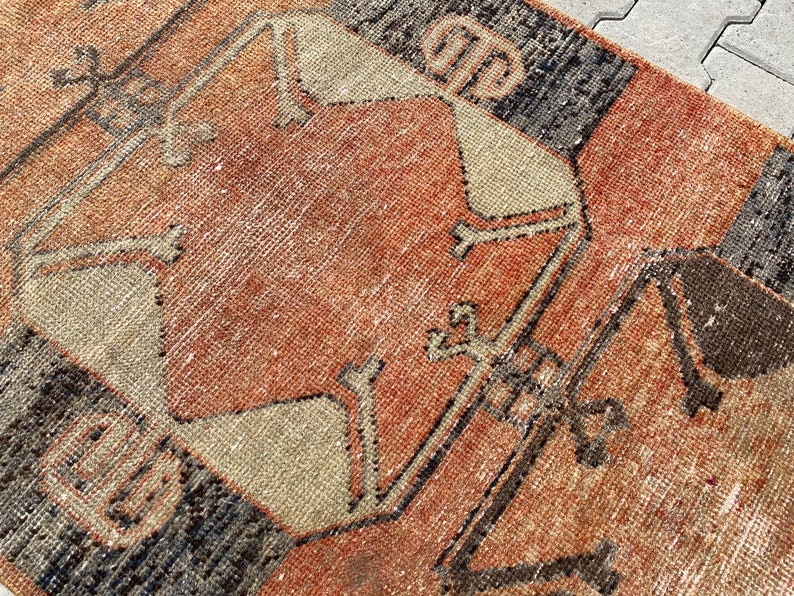 Pu&ograve; includere: Un tappeto vintage con un motivo geometrico in tonalit&agrave; di marrone, arancione e beige. Il tappeto ha un aspetto usurato e sbiadito, che gli conferisce un aspetto rustico e antico.