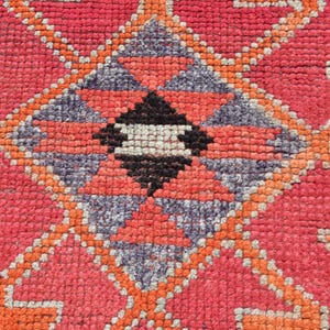May include: Close-up of a red, orange, and gray patterned rug with a geometric design. The rug is woven with a variety of textures and colors.