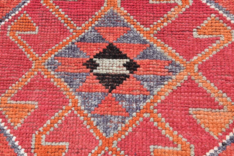 May include: Close-up of a red, orange, and gray patterned rug with a geometric design. The rug is woven with a variety of textures and colors.
