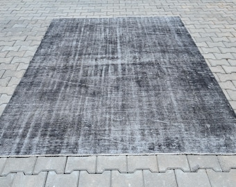 May include: A rectangular, distressed-look rug in shades of black and gray. The rug has a faded appearance with a textured surface, suggesting a vintage or antique style. The rug is placed on a gray brick surface.