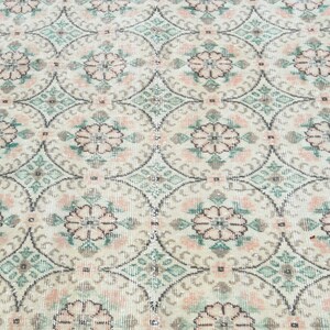 May include: A close-up of a white rug with a repeating pattern of pink and green floral designs.