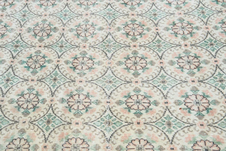 May include: A close-up of a white rug with a repeating pattern of pink and green floral designs.