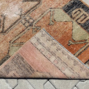 Pu&ograve; includere: Un tappeto vintage con un motivo geometrico in tonalit&agrave; di marrone, beige e nero. Il tappeto &egrave; piegato a met&agrave;, mostrando il retro, che &egrave; di colore beige pi&ugrave; chiaro.