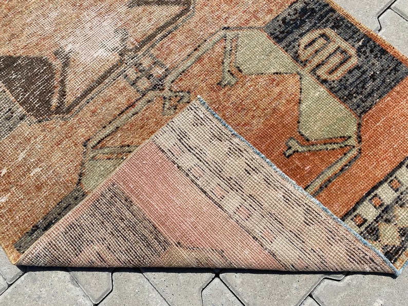 Pu&ograve; includere: Un tappeto vintage con un motivo geometrico in tonalit&agrave; di marrone, beige e nero. Il tappeto &egrave; piegato a met&agrave;, mostrando il retro, che &egrave; di colore beige pi&ugrave; chiaro.