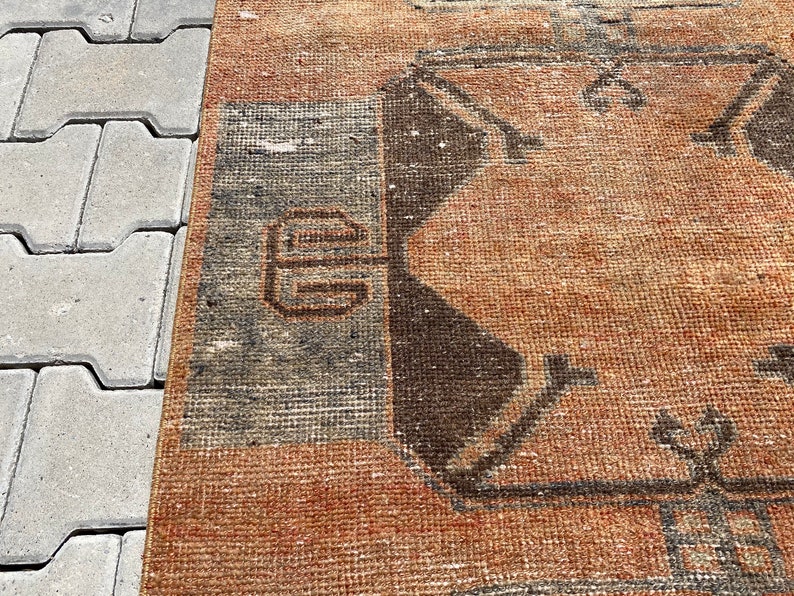 Pu&ograve; includere: Primo piano di un tappeto marrone e grigio con un design geometrico. Il tappeto ha un aspetto usurato e vintage.