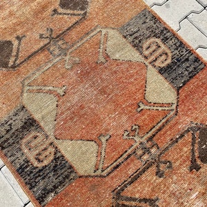 Pu&ograve; includere: Un tappeto vintage con un motivo geometrico in tonalit&agrave; di marrone, beige e rosso. Il tappeto ha un aspetto vissuto ed &egrave; fatto di lana.