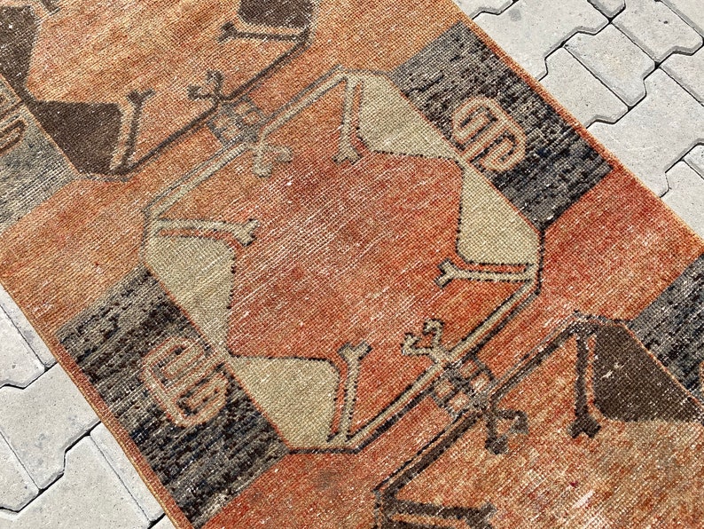 Pu&ograve; includere: Un tappeto vintage con un motivo geometrico in tonalit&agrave; di marrone, beige e rosso. Il tappeto ha un aspetto vissuto ed &egrave; fatto di lana.