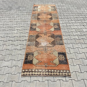Pu&ograve; includere: Un tappeto lungo e stretto con un motivo geometrico in tonalit&agrave; di marrone, arancione e beige. Il tappeto ha frange su entrambi i lati.