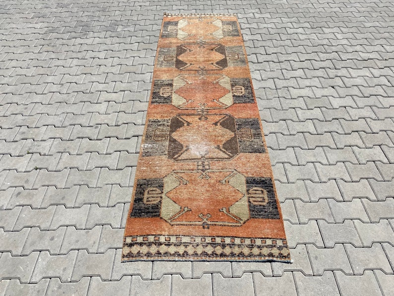 Pu&ograve; includere: Un tappeto lungo e stretto con un motivo geometrico in tonalit&agrave; di marrone, arancione e beige. Il tappeto ha frange su entrambi i lati.