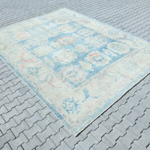 K&ouml;nnte beinhalten: Ein Vintage-Teppich mit hellblauem Hintergrund und cremefarbenem Muster. Der Teppich hat ein geometrisches Design mit floralen Motiven und einem Rand.