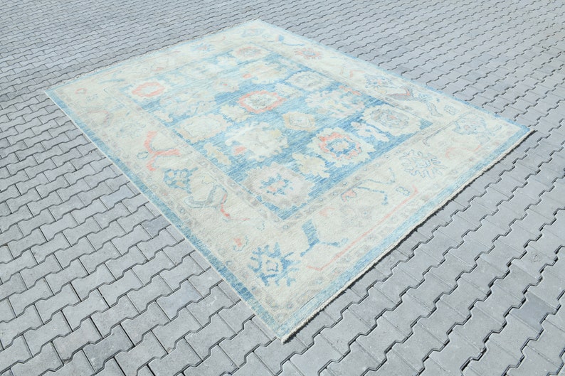 K&ouml;nnte beinhalten: Ein Vintage-Teppich mit hellblauem Hintergrund und cremefarbenem Muster. Der Teppich hat ein geometrisches Design mit floralen Motiven und einem Rand.