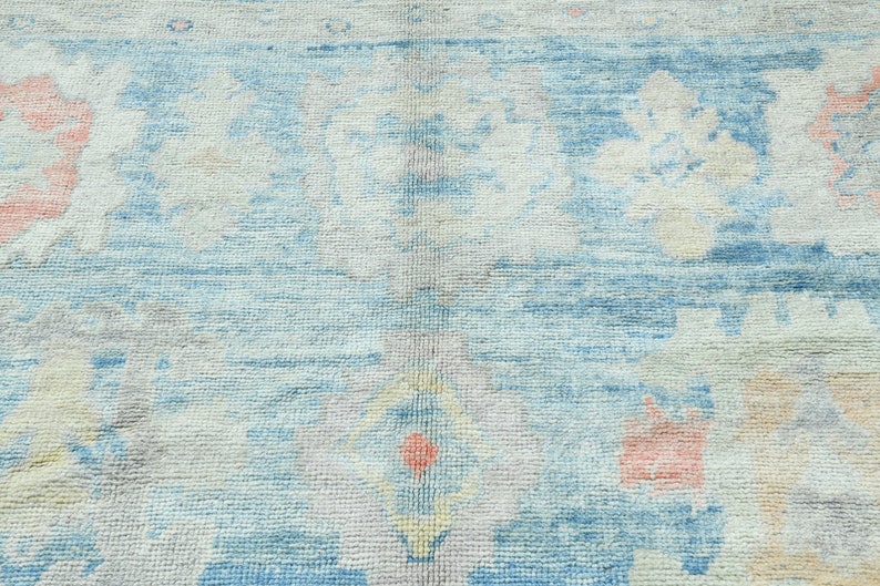 K&ouml;nnte beinhalten: Ein hellblauer Teppich mit einem verblassten Blumenmuster in Rosa-, Gelb- und Wei&szlig;t&ouml;nen.
