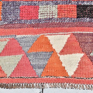 May include: A colorful woven rug with a geometric pattern of triangles in shades of red, orange, white, and gray. The rug has a fringe border.