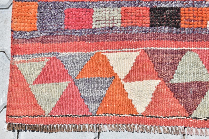 May include: A colorful woven rug with a geometric pattern of triangles in shades of red, orange, white, and gray. The rug has a fringe border.
