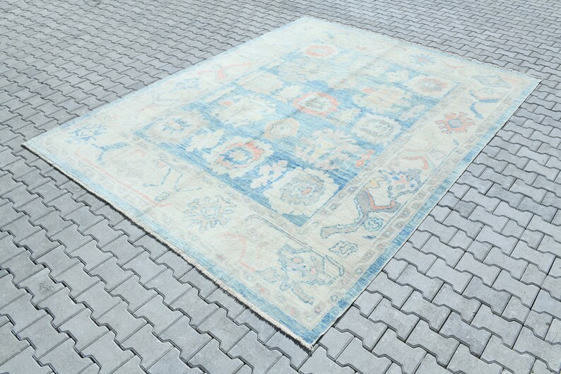 K&ouml;nnte beinhalten: Ein Vintage-Teppich mit hellblauem Hintergrund und cremefarbenem Rand. Der Teppich hat ein florales Muster in Blaut&ouml;nen, Rosa und Creme.