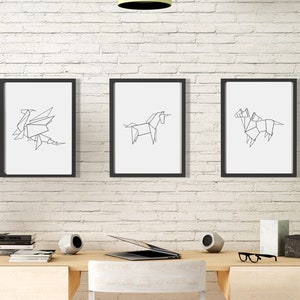 May include: Three black framed prints of line drawings of origami animals on a white brick wall above a wooden desk with a laptop, two speakers, and a plant.